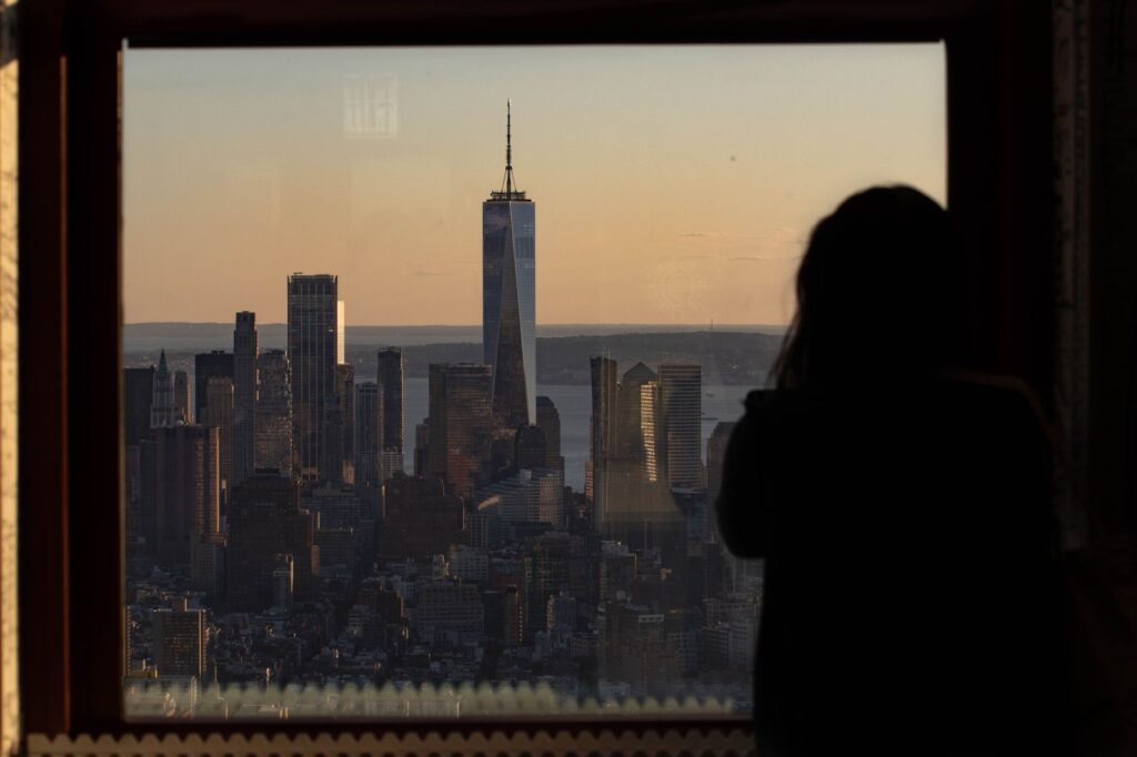 Silhouette of a person observing One World Trade Center from a window at sunset in New York City.