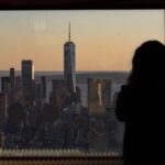 Silhouette of a person observing One World Trade Center from a window at sunset in New York City.