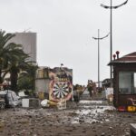 City street filled with storm debris and damaged structures under a cloudy sky.