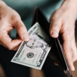 Closeup of crop male in casual clothes taking dollars out of wallet while paying in shop