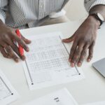 An educator carefully checks exam papers using a red marker at a desk, illustrating focused grading.