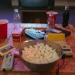 A nostalgic setup with popcorn, VHS tapes, and retro gaming consoles on a wooden table.