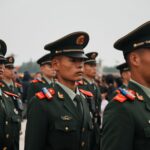 Close-up of military personnel in green uniforms and hats during a parade.