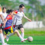 Women playing soccer on a vibrant green field in Hanoi, Vietnam. Team sports and outdoor activity.