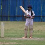 A young female cricket player poised to bat on a grassy field in Gahunje, India.