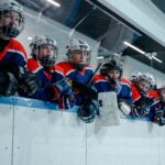 A junior ice hockey team waits eagerly at the rink edge, embodying teamwork and anticipation.