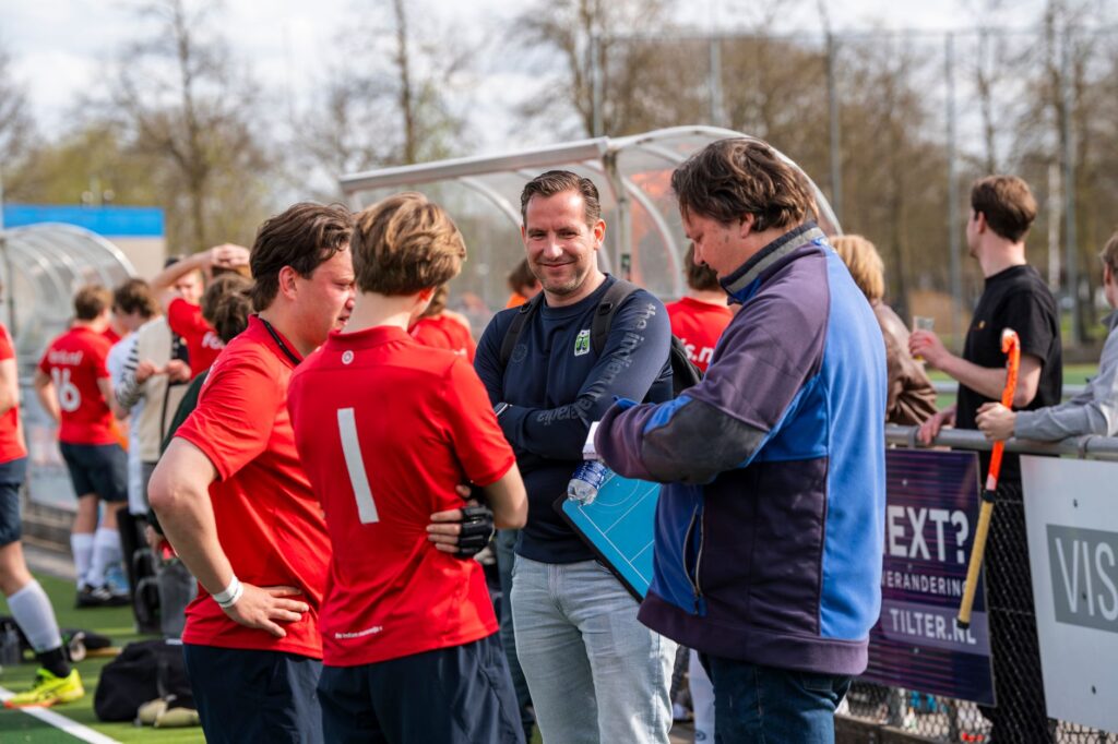 Field hockey players discussing strategy with coaches outdoors during a match.