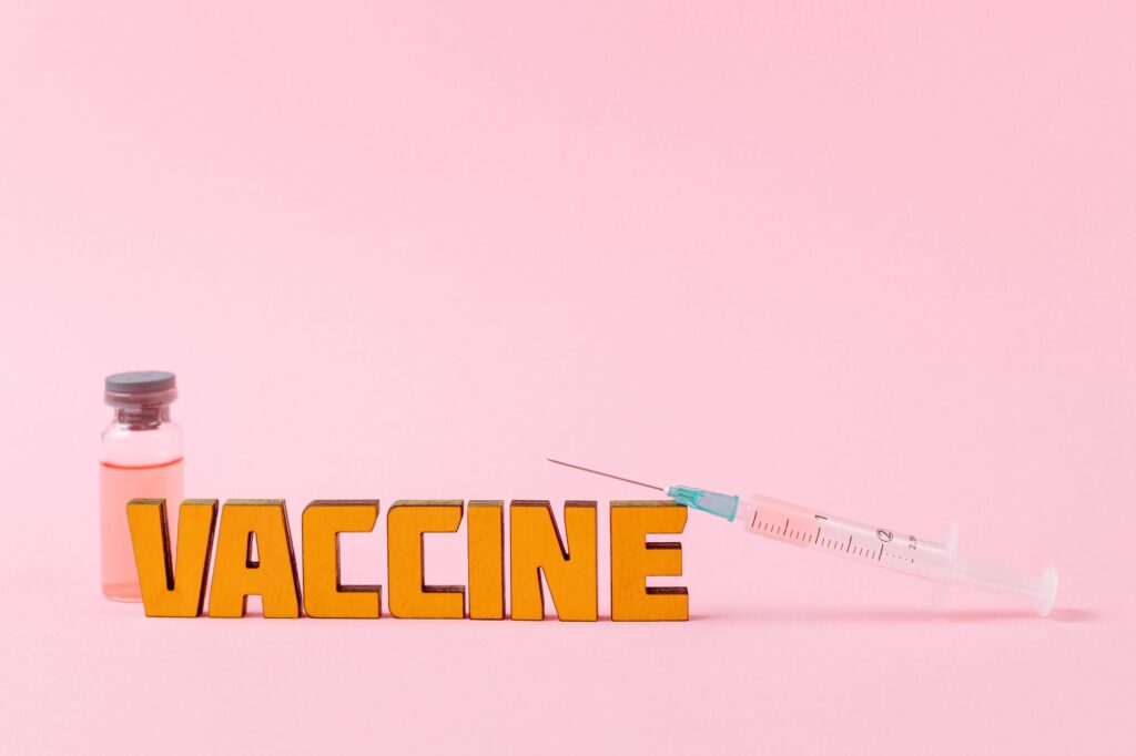 Close-up of a syringe and vaccine vial on a pink backdrop for health concepts.