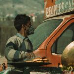 A street vendor wearing a mask prepares food outdoors, reflecting the ongoing pandemic.