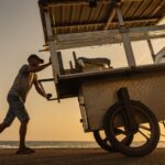 A street vendor pushes a food cart along the beach in Colombo during a stunning sunset.