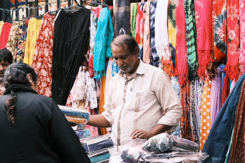 A lively street market in Bengaluru with vibrant fabrics and interactions between vendors and customers.