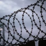 A dramatic view of barbed wire silhouetted against a cloudy sky, capturing themes of security and confinement.