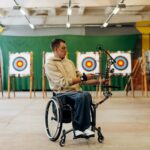 Man in a wheelchair practicing archery indoors, demonstrating skill and determination.