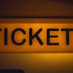 Close-up of an illuminated yellow ticket sign against a dark background.