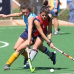 Two female field hockey players compete fiercely on an outdoor turf field.