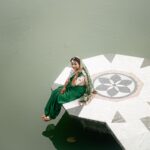 A woman in vibrant traditional Bangladeshi attire sits gracefully on a platform over water.