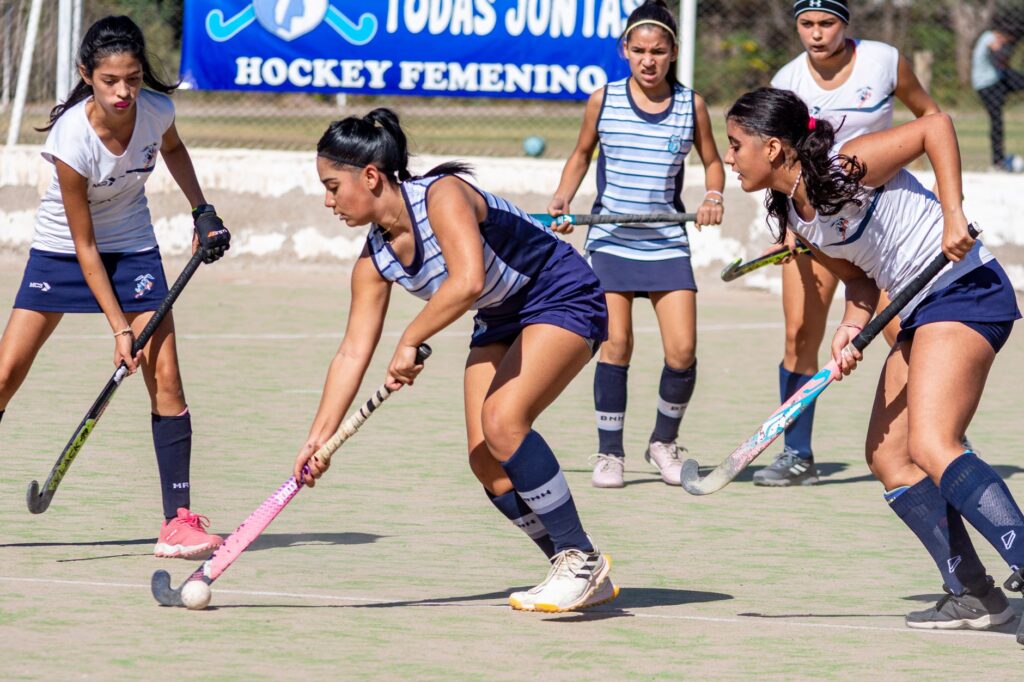 Female athletes engaged in a dynamic field hockey match, showcasing teamwork and competitive spirit.