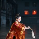 Woman in a traditional Japanese costume with makeup, performing indoors.