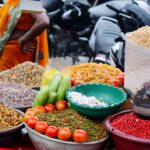 Colorful outdoor market stall featuring spices, tomatoes, cucumbers, and other vegetables.