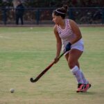 Female field hockey player in action on the field, demonstrating skill and focus.
