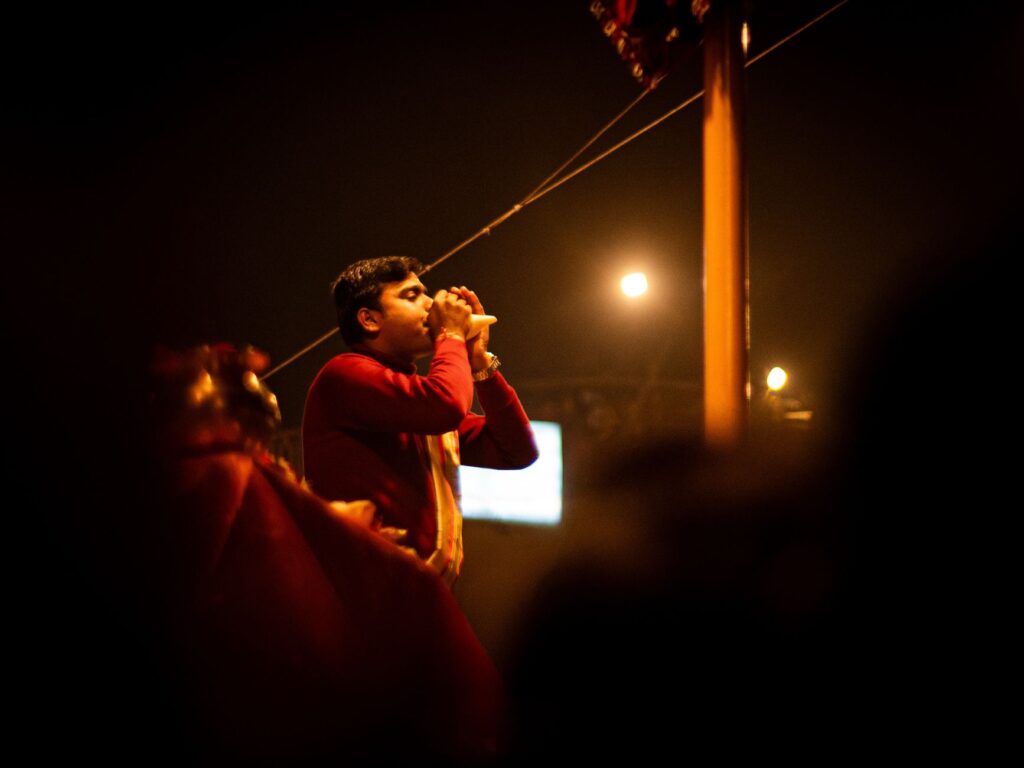 A young man participates in a traditional religious ceremony at night in Varanasi, India, blowing a conch shell with devotion.