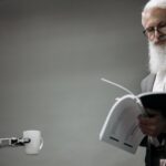 Elderly man reads as a robotic arm holds a coffee cup, showcasing technology integration.