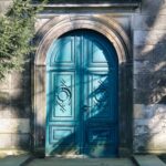 A vibrant blue arched door with gothic designs. Shadows of trees add depth.