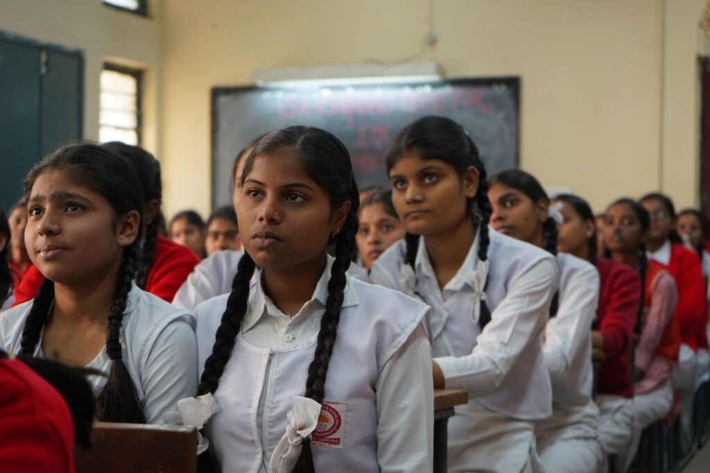 Group of Indian schoolgirls attentively listening in their classroom wearing uniforms.