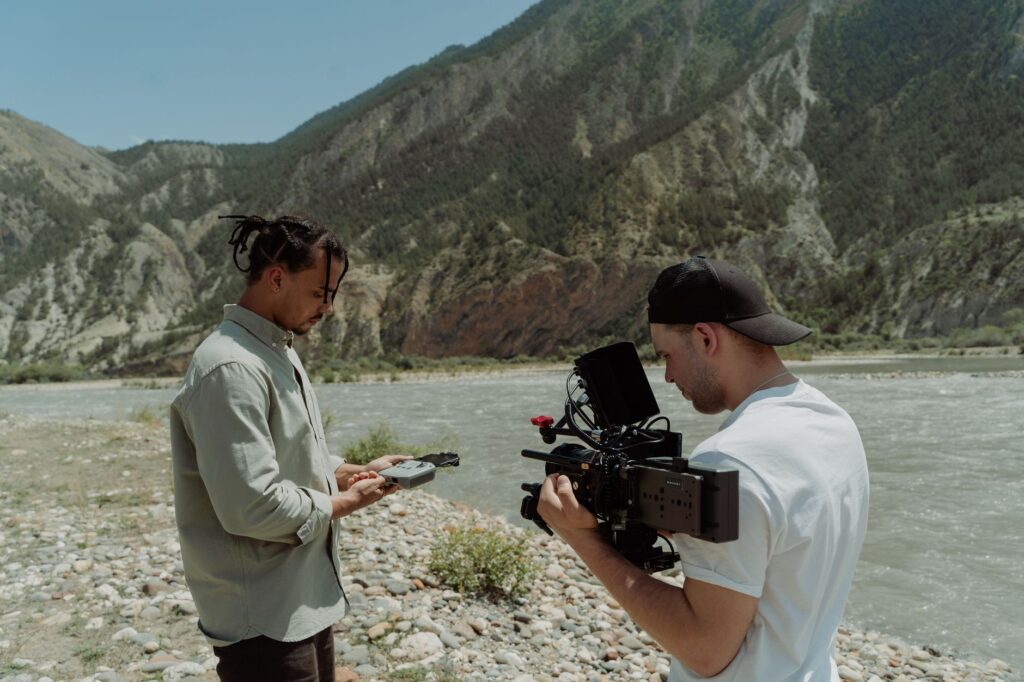 Two filmmakers capture scenic mountain river with professional camera.