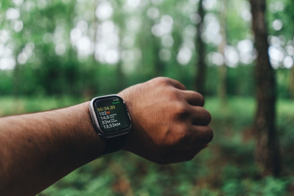 Close-up of a hand wearing a smartwatch with blurred forest background, showing fitness metrics.