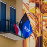 A vibrant urban balcony with flags against a mural backdrop in daylight.