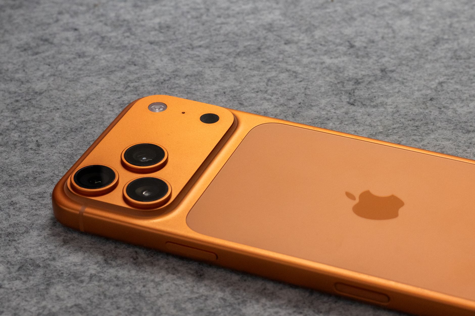 Orange smartphone with dual cameras placed on a soft gray fabric surface.