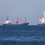 Two container ships sailing in the open sea, under a clear blue sky, captured in bright daylight.