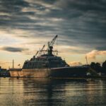 A military vessel docked at Marinette Harbor during a dramatic sunset with overcast clouds.