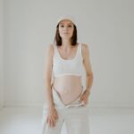 Pregnant woman in white clothing posing indoors with a serene expression.