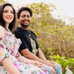 Happy couple sitting together outdoors, smiling amid greenery.