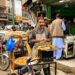 Bustling street scene with vendor frying kebabs in Mingora's busy bazaar, Pakistan.