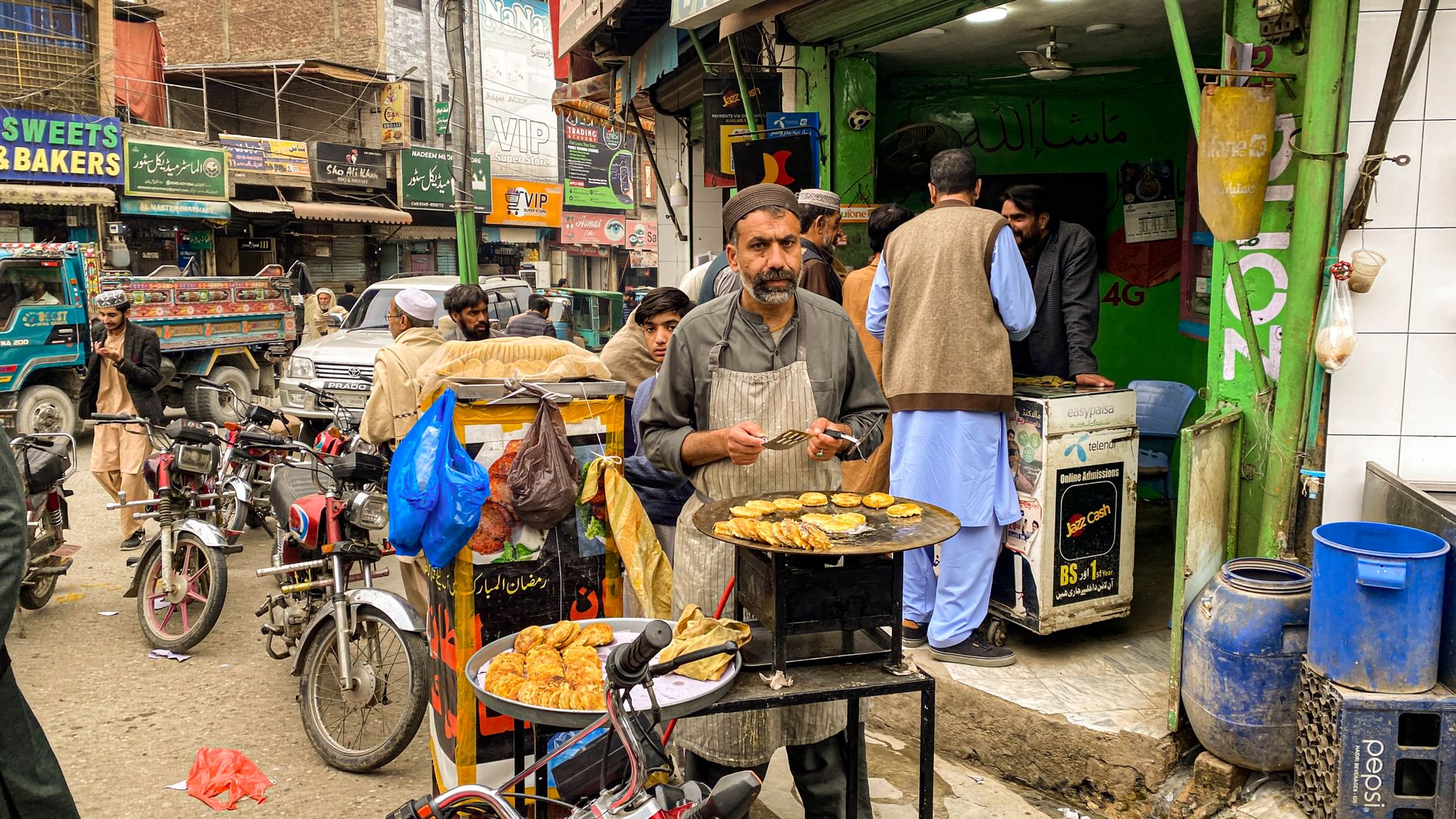 Bustling street scene with vendor frying kebabs in Mingora's busy bazaar, Pakistan.
