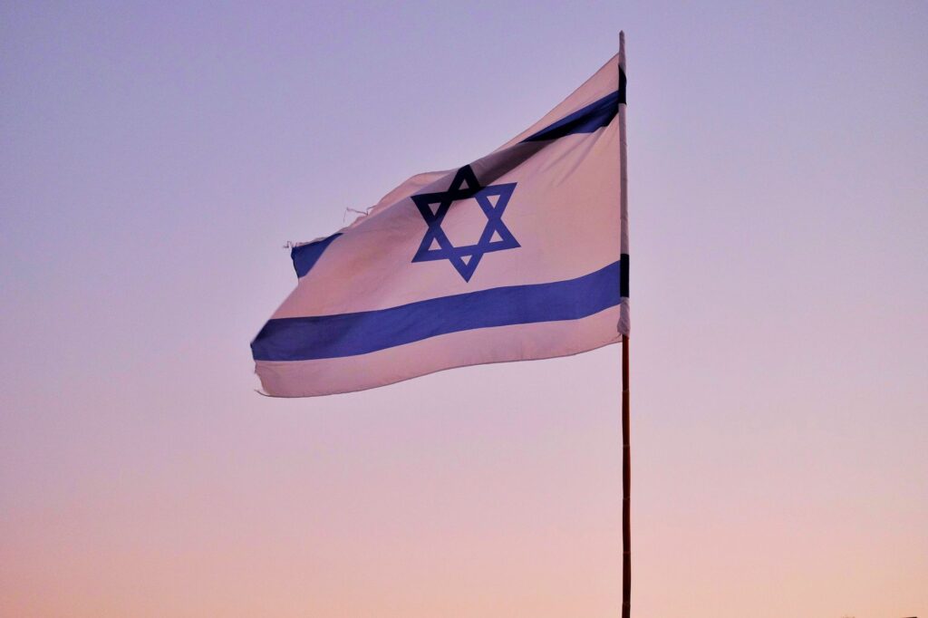 Israeli flag on a flagpole against a serene sunset sky, symbolizing national pride.
