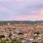 A panoramic view of Jaipur, Rajasthan during sunset, showcasing a blend of urban structures and natural landscape.