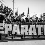 A group of people marching for reparations holding a large banner on a city street.