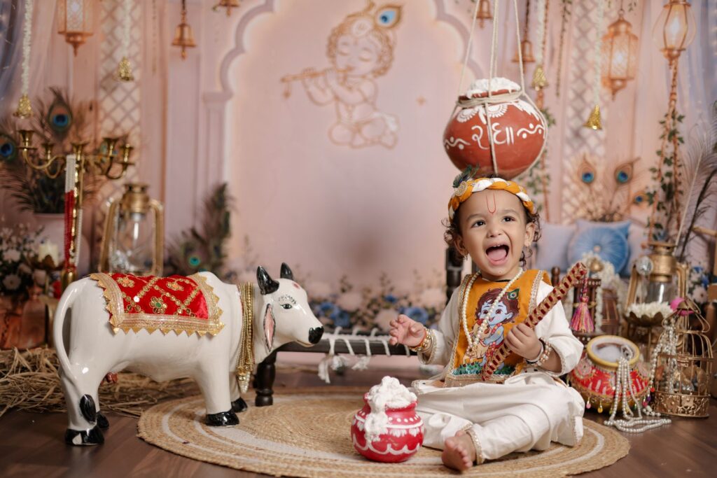 Joyful child in traditional attire with festive decor celebrating Janmashtami indoors.