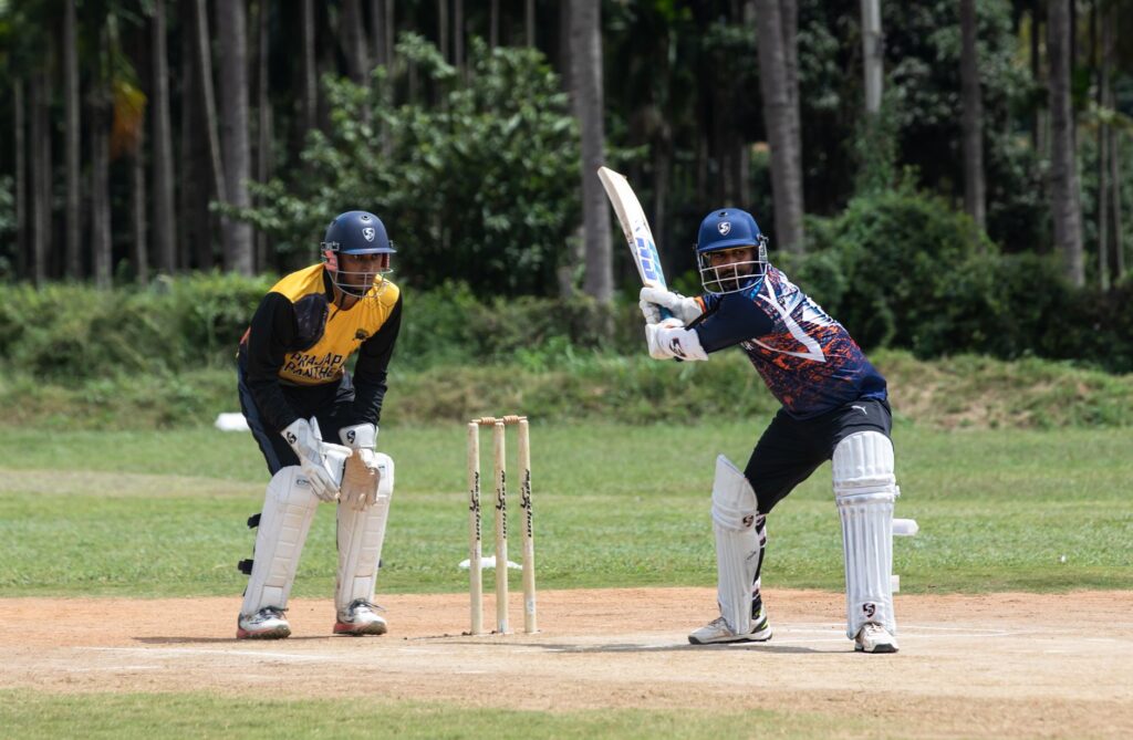 Cricketer ready to bat with wicketkeeper in sports gear outdoors.