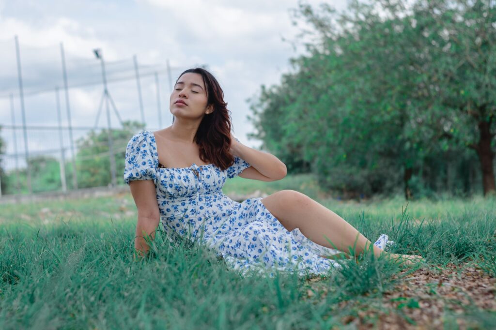 A serene portrait of a woman in a floral dress sitting on grass, enjoying a summer day outdoors.