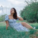 A serene portrait of a woman in a floral dress sitting on grass, enjoying a summer day outdoors.
