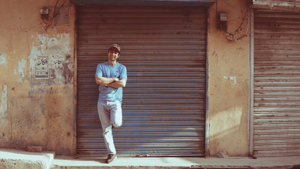 Man in blue shirt posing casually against a roller shutter in Sialkot, Pakistan.