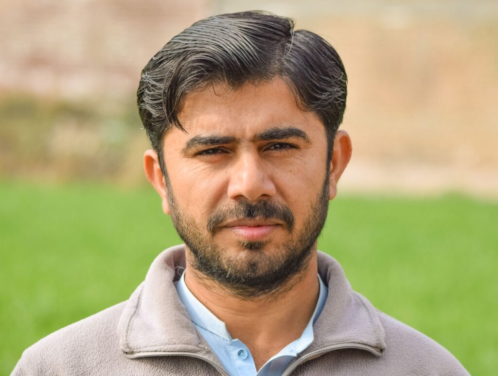 Close-up portrait of a bearded man in a field, looking directly at the camera.