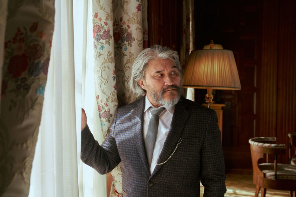 Elderly man gazing thoughtfully in a luxurious, vintage-style living room.