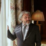Elderly man gazing thoughtfully in a luxurious, vintage-style living room.