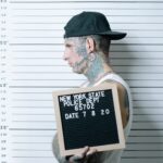 Side view of tattooed man holding mugshot board in police lineup.
